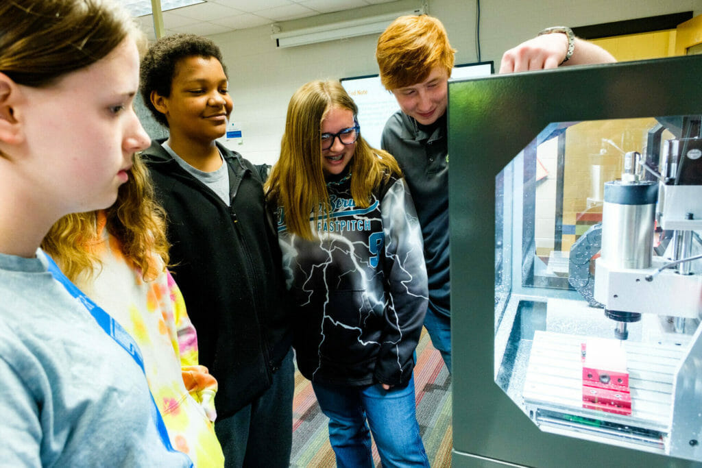 Middle school students and an instructor look at a 3-d printer