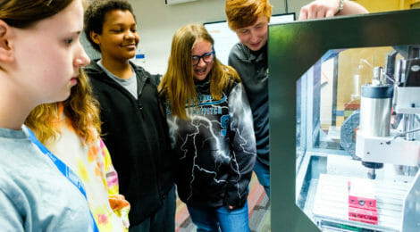 Middle school students and an instructor look at a 3-d printer