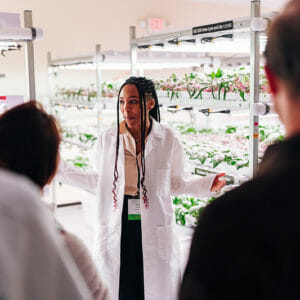 A woman in a lab coat talks to a group about controlled environment agriculture