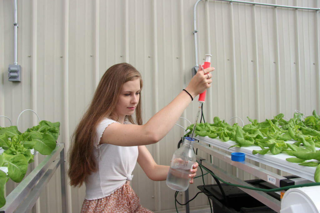 An female intern works with plants and a syringe.