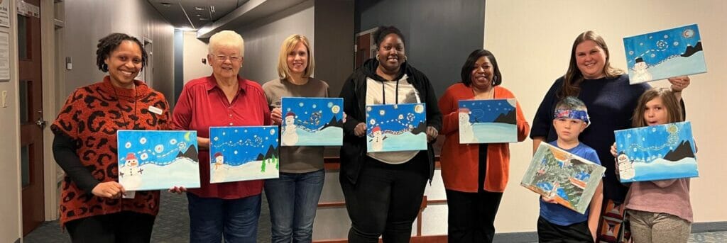 A group of people pose with paintings that they finished in a Wonder Community class. 