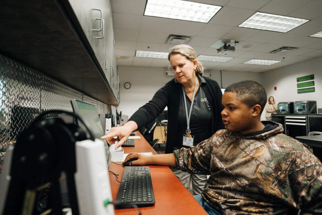 A GO TEC teacher assists a male middle school student on a computer. 