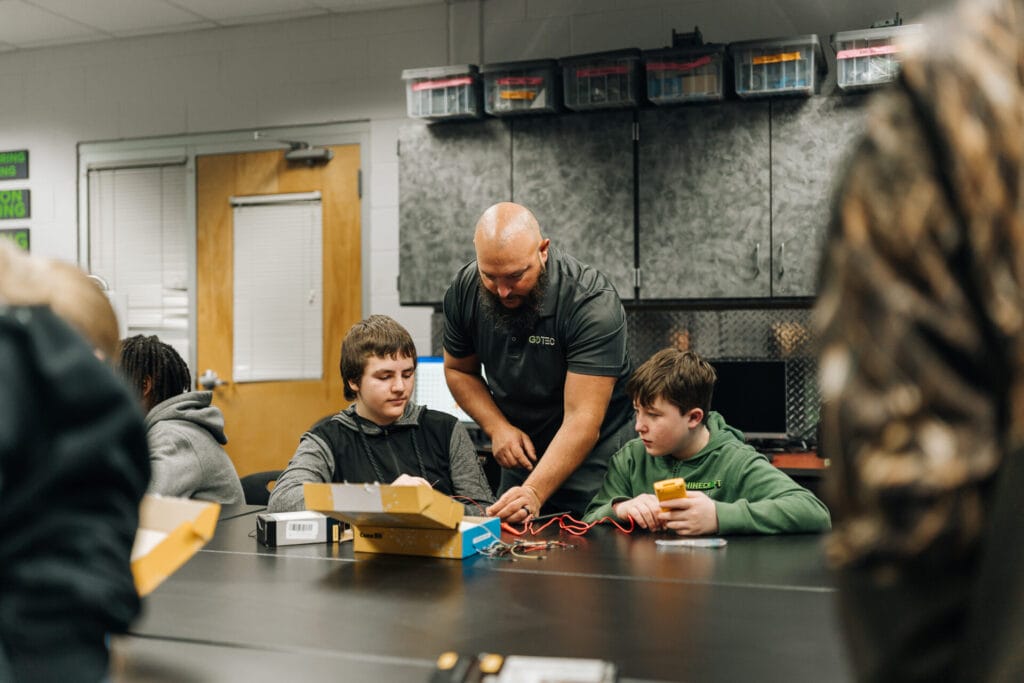 A GO TEC instructor helps students with a project involving electrical wiring. 