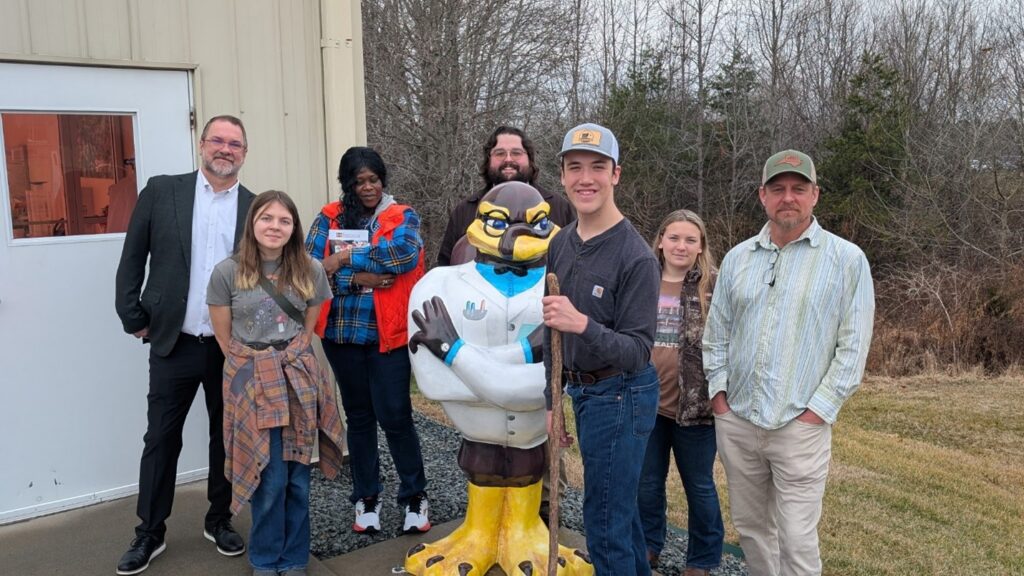 A group of people pose together with a statue of a Virginia Tech Hokie Bird. 