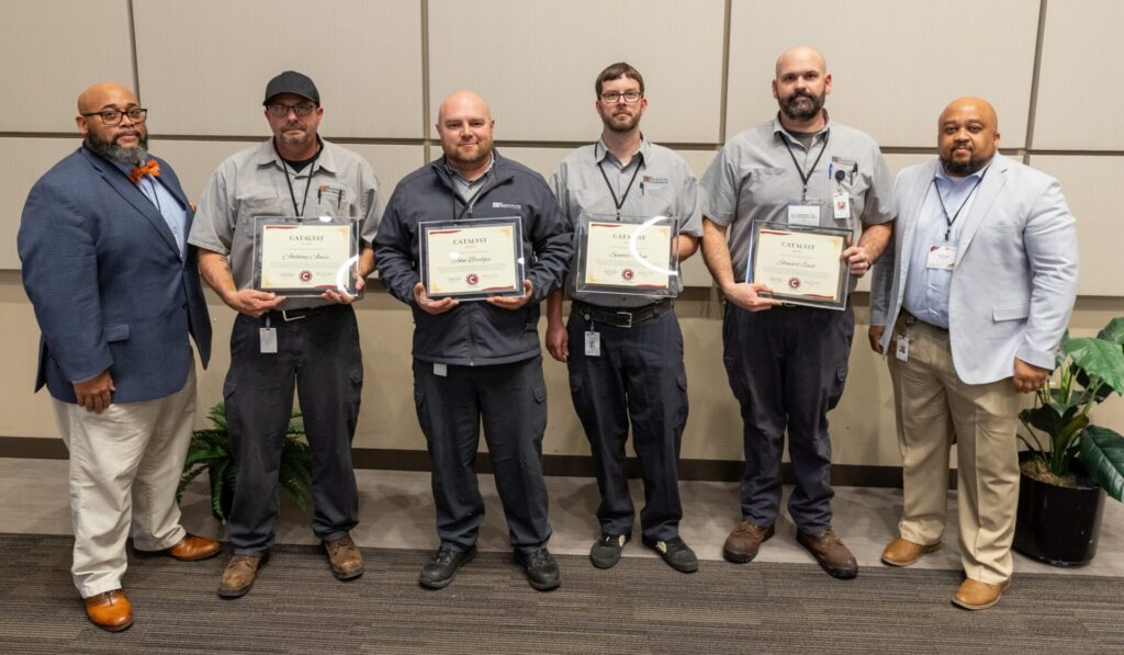A group of six people smiles at the camera. The two in the middle are holding awards.