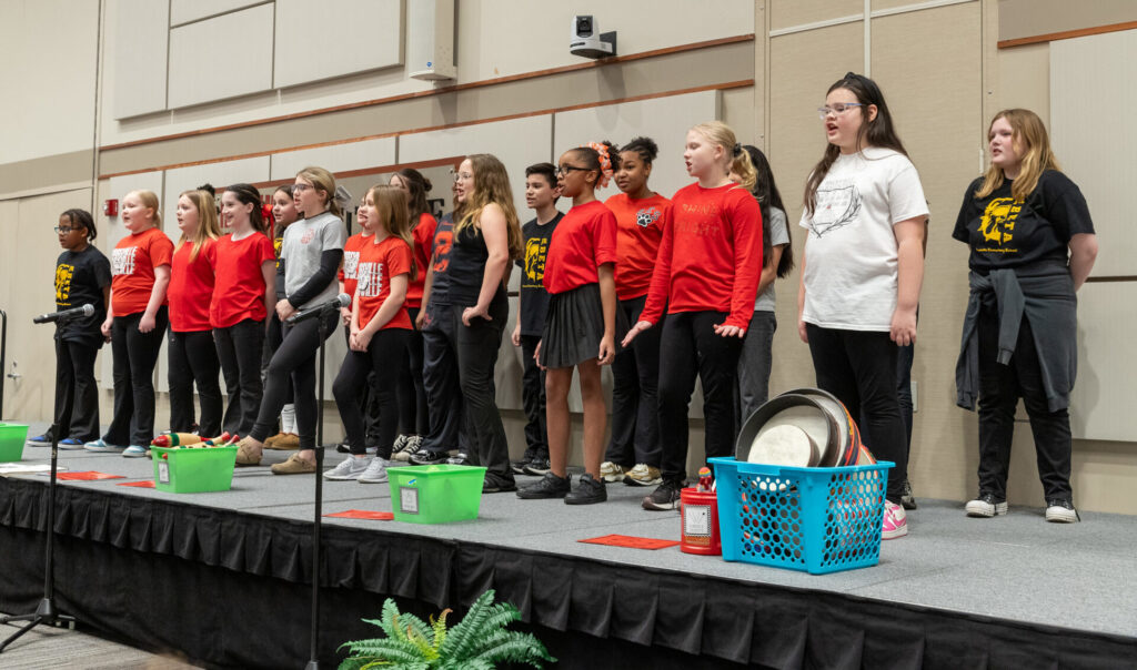 A group of students in mostly red shirts sing on a stage.