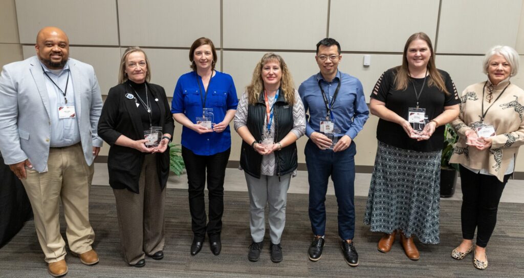 A group of several people hold service milestone award trophies and smile.